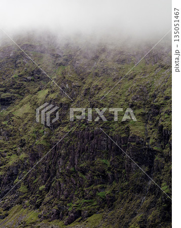 Green rocky mountain side in County Kerry, Ireland, with fog at the top of the peak. 135051467
