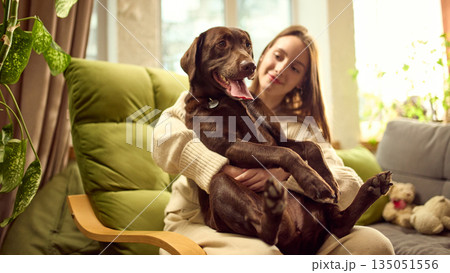 Woman holding dog in her arms while sitting on sofa at home Woman holding dog in her arms while sitting on sofa at home 135051556