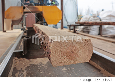 Sawing of wooden logs. The log is sawn on a machine. A woodworking machine. Wood processing workshop. Carpentry work. 135051991