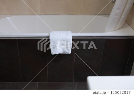 A foot towel is hanging on the edge of the tub. Bathroom. White terry towel. The concept of cleanliness and order. 135052017