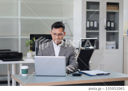 Businessman using laptop computer and smartphone in office. Happy man, entrepreneur, small business owner working online. 135052061