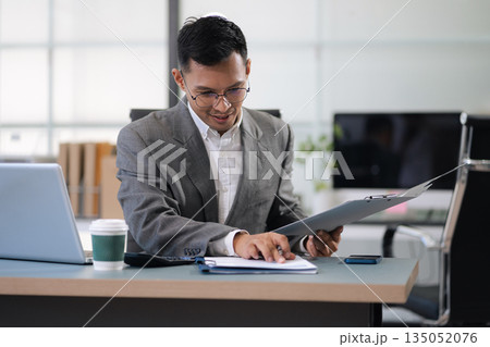Mature businessman calculate and analyzing graph document financial with report and laptop in office. Mature businessman calculate and analyzing graph document financial with report and laptop in office. 135052076