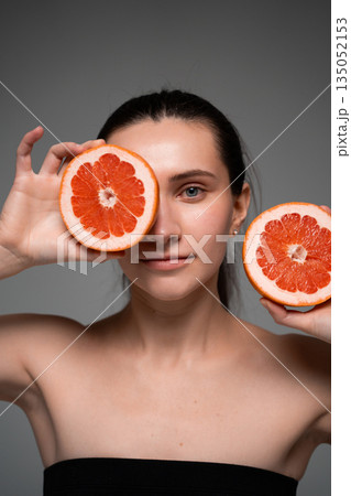 Smiling woman holding fresh grapefruit halves near face on neutral background, healthy lifestyle, natural beauty, vitamins, wellness concept Smiling woman holding fresh grapefruit halves near face on neutral background, healthy lifestyle, natural beauty, vitamins, wellness concept 135052153