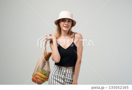 Woman posing with reusable textile shopping bag and fresh groceries, sustainable living and eco friendly consumption concept in studio 135052165