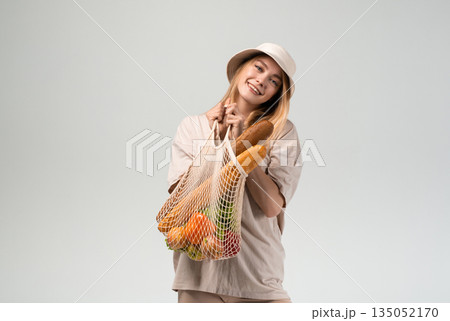 Young woman holding reusable mesh shopping bag with vegetables, fruits and bread, minimal sustainable lifestyle and eco friendly shopping concept Young woman holding reusable mesh shopping bag with vegetables, fruits and bread, minimal sustainable lifestyle and eco friendly shopping concept 135052170