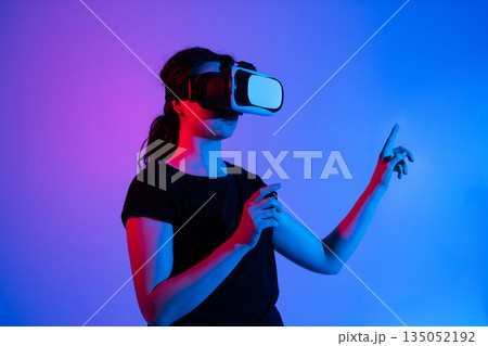 Woman wearing virtual reality headset and interacting with virtual space using both hands in futuristic neon studio environment Woman wearing virtual reality headset and interacting with virtual space using both hands in futuristic neon studio environment 135052192