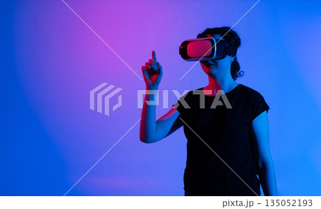 Woman pointing upward while using virtual reality headset, immersive technology, digital interaction, futuristic interface, innovation and modern experience Woman pointing upward while using virtual reality headset, immersive technology, digital interaction, futuristic interface, innovation and modern experience 135052193