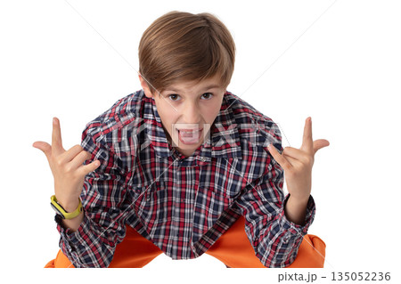 Teenage boy in plaid shirt and orange pants clenches fist and sticks out tongue. Difficult teenage years. Teenage boy in plaid shirt and orange pants clenches fist and sticks out tongue. Difficult teenage years. 135052236