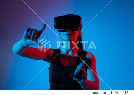 Woman wearing VR headset pointing forward, gesture based interaction with virtual reality technology 135052323