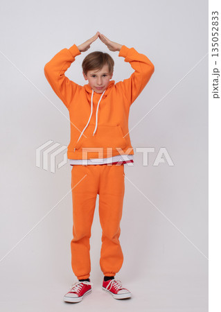 A boy in an orange sweatshirt and orange pants holds his hands in a roof-over-head pose. A boy in an orange sweatshirt and orange pants holds his hands in a roof-over-head pose. 135052833