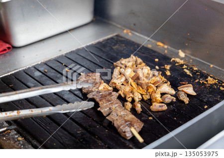 A person is cooking anticuchos on a grill A person is cooking anticuchos on a grill 135053975