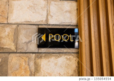 Directional pool sign mounted on stone wall indoors. Clear wayfinding design, guest orientation, and functional hospitality communication enhancing relaxed resort navigation. Directional pool sign mounted on stone wall indoors. Clear wayfinding design, guest orientation, and functional hospitality communication enhancing relaxed resort navigation. 135054554