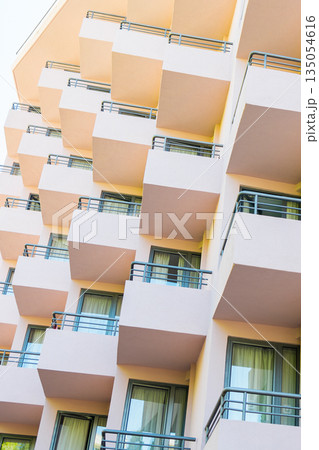 Repetitive balconies on modern building facade with soft pastel tones. Architectural rhythm, urban living aesthetics, and structured design shaping contemporary residential environments. 135054616