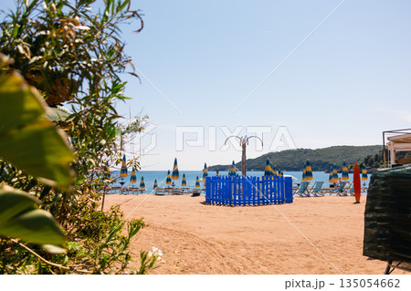 Beach area with sun umbrellas and outdoor shower near sea. Coastal recreation infrastructure, relaxed vacation rhythm, and open seaside spaces encouraging summer leisure. Beach area with sun umbrellas and outdoor shower near sea. Coastal recreation infrastructure, relaxed vacation rhythm, and open seaside spaces encouraging summer leisure. 135054662