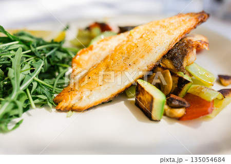 Grilled fish fillet with vegetables served on restaurant plate. Healthy nutrition, balanced diet choices and mindful dining habits supporting modern lifestyle wellbeing. Grilled fish fillet with vegetables served on restaurant plate. Healthy nutrition, balanced diet choices and mindful dining habits supporting modern lifestyle wellbeing. 135054684