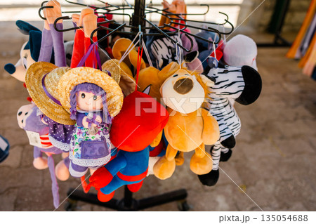 Hanging plush dolls and animal toys at beach market. Childhood nostalgia, souvenir culture, playful retail, and summer tourism atmosphere 135054688