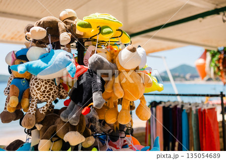 Plush animal toys hanging at seaside souvenir. Children merchandise, tourism retail, playful design, and colorful coastal market scene 135054689