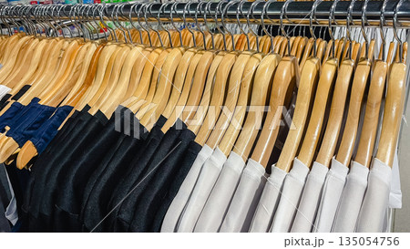 Row of black, white and navy blue t-shirts hanging on wooden hangers on a metal rack in a clothing store Row of black, white and navy blue t-shirts hanging on wooden hangers on a metal rack in a clothing store 135054756