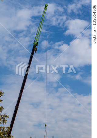 Photo of a construction truck crane, the retractable boom of which is lengthened at the end by a telescopic extension device - a jib. Vertical shot against blue sky background with clouds 135054906