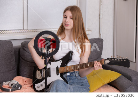 Young musician playing electric guitar and recording tutorial at home during bright afternoon 135055030