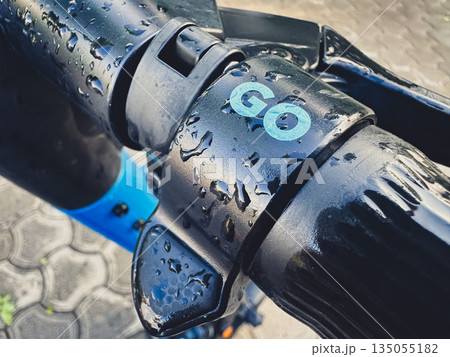 Close-up of a wet electric scooter handlebar with 'GO' text. Close-up of a wet electric scooter handlebar with 'GO' text. 135055182