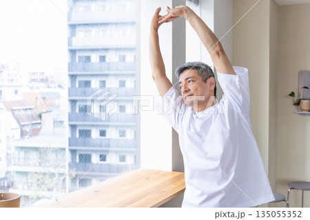 窓辺でストレッチをするシニア男性 窓辺でストレッチをするシニア男性 135055352