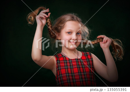 A girl in a red checkered dress and long braids. She smiles. She holds her hair up. A girl in a red checkered dress and long braids. She smiles. She holds her hair up. 135055391