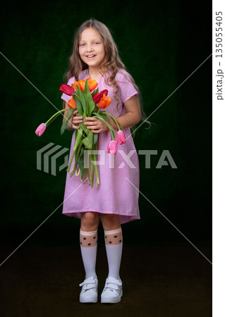 A girl with a funny expression holds a bouquet of tulips. She smiles on a dark background. A girl with a funny expression holds a bouquet of tulips. She smiles on a dark background. 135055405