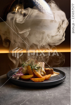 Appetizing smoked dish with roasted potatoes, decorated with rosemary on dark plate, steam rising elegantly, fine dining concept 135057577