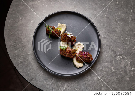 Exquisite presentation of gourmet beef tartare topped with herbs and flowers on smoked mayonnaise, food styling concept 135057584