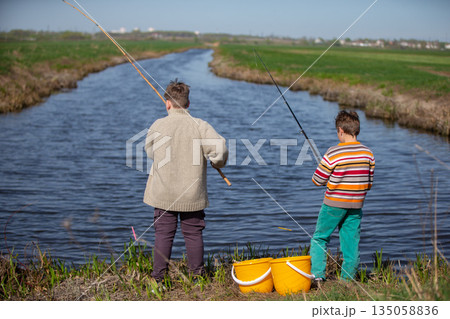 Boys children catch fish near the river. View from behind. Boys children catch fish near the river. View from behind. 135058836