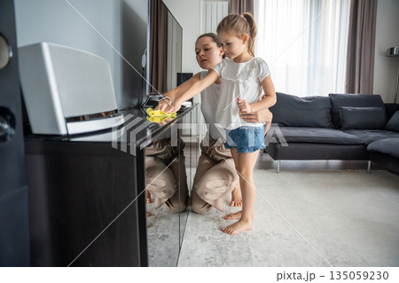 Mother and daughter wiping TV stand together at home. Everyday household routine and shared responsibility in real life interior 135059230