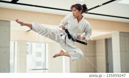 室内で高く跳び上がり回し蹴りを放つ日本人女性の空手家 室内で高く跳び上がり回し蹴りを放つ日本人女性の空手家 135059247