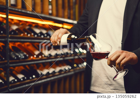 Faceless Man Pouring Red Wine into Glass in Cellar Faceless Man Pouring Red Wine into Glass in Cellar 135059262