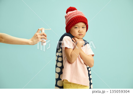 Frustrated and ill child with a dissatisfied expression doesn't want gets bitter cough medicine from adult hand, standing on blue isolated 135059304