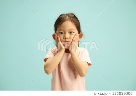 Shocked Five Year Old Child Girl Holding Face and Expresses Surprise Looking to Camera Stands on Blue Isolated 135059306