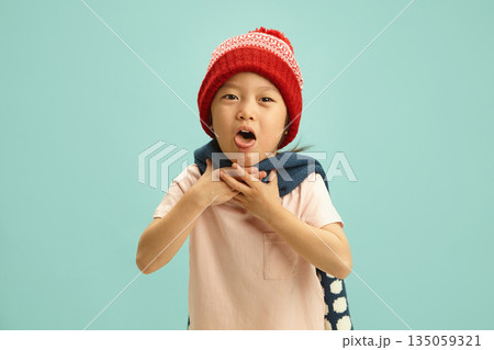 Sick Chinese apperance child with a ill throat having acute coughing attack, wearing in winter hat, woolen scarf is wrapped around her neck, difficult for her to breathe, she clutches at her throat 135059321