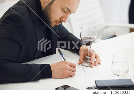 Focused Sommelier in Black Attire Analyzing Wine Color ad Taking Notes at Professional Tasting Course 135059323