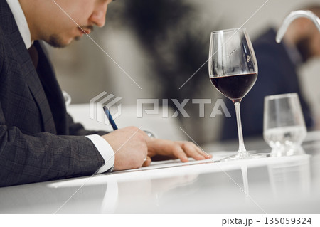 ProfessionalFaceless Sommelier Evaluating Red Wine by Tasting it and Making Notes to Wine Card of Participant. Wine study school, winemaking lecture. ProfessionalFaceless Sommelier Evaluating Red Wine by Tasting it and Making Notes to Wine Card of Participant. Wine study school, winemaking lecture. 135059324