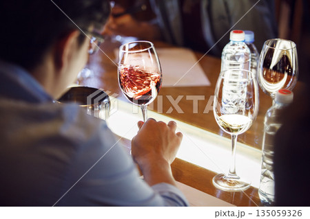 Sommelier Tasting Glass of Red Wine, Swirling it Sitting at Table 135059326