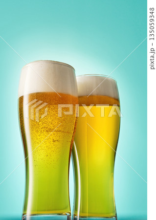Two glasses with foamy beer on light blue background. Two glasses with foamy beer on light blue background. 135059348