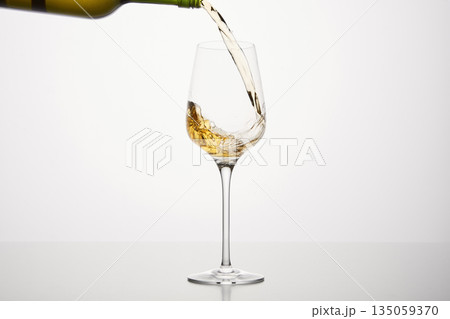 White alcohol beverage flows to wineglass, close up on white isolated. White alcohol beverage flows to wineglass, close up on white isolated. 135059370