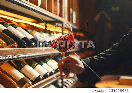 Hand Holding Swirled Red Wineglass by Racks 135059478
