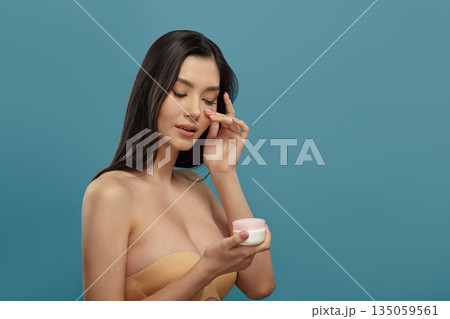 Well-groomed girl holds round white cream jar with pink lid 135059561