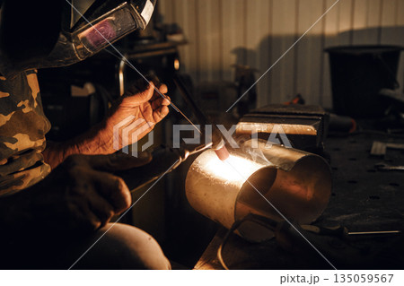 Male in face mask welds with argon welding. Industrial welder worker welding using argon machine, close up. Man working with arc welding machine in garage. 135059567