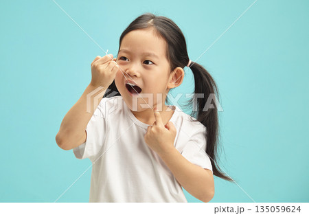 Korean sweet little girl cleaning her teeth with a dental floss on blue isolated.  135059624