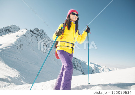 Smiling Woman Hiking in Snowy Mountains With Trekking Poles During Winter 135059634