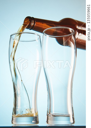 Lager, ale flows to empty tall glasses from bottle. Lager, ale flows to empty tall glasses from bottle. 135059661