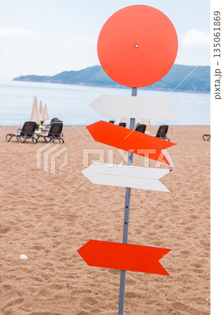 Wooden beach signpost with arrows on seaside promenade, copy space. Summer vacation, coastal leisure, and travel direction concept. Wooden beach signpost with arrows on seaside promenade, copy space. Summer vacation, coastal leisure, and travel direction concept. 135061869