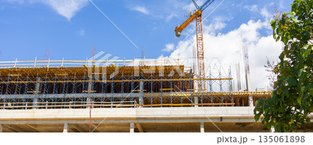 Concrete building under construction with scaffolding and crane. Urban infrastructure, civil engineering, and ongoing development in modern architecture. 135061898